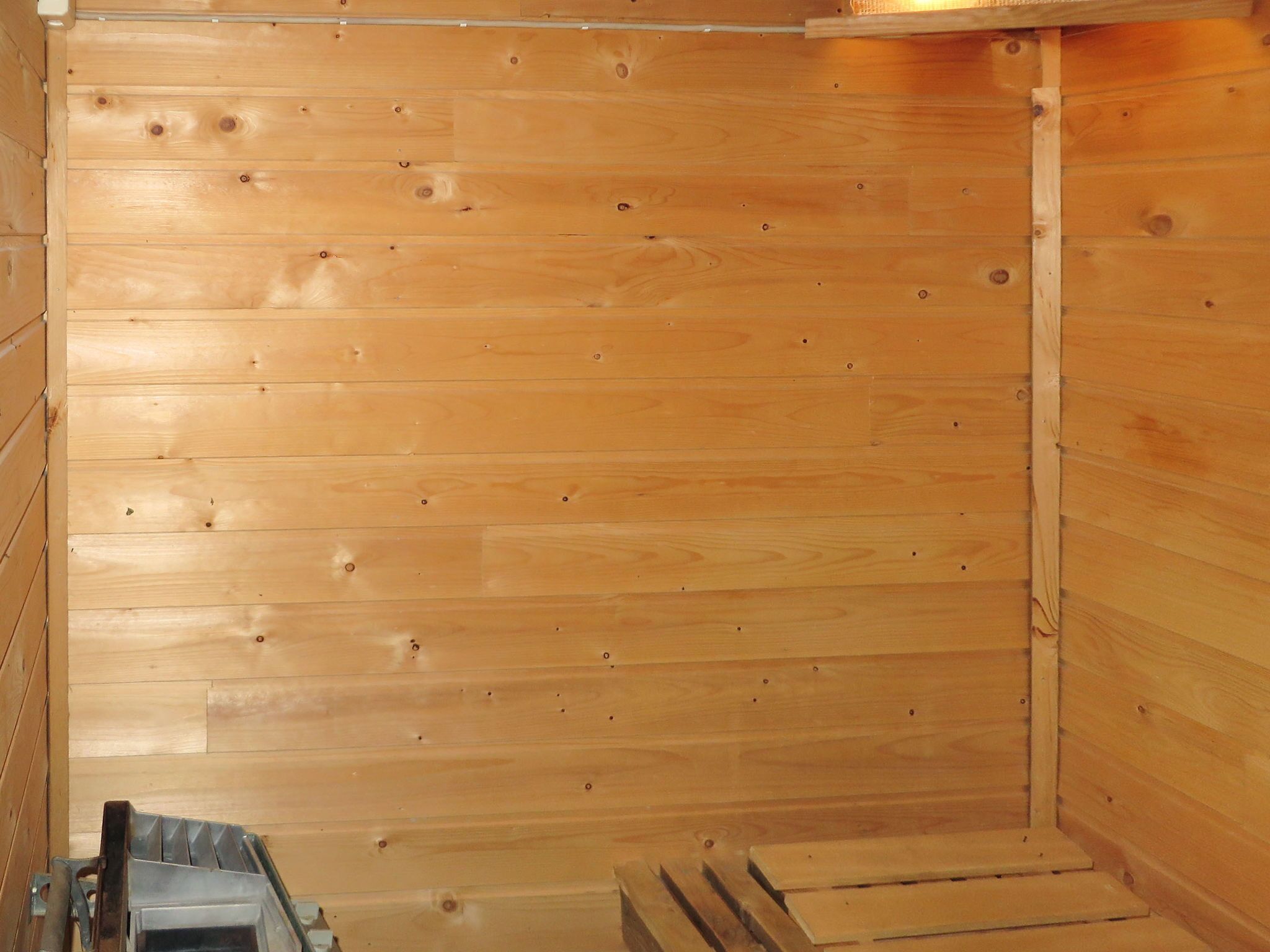 A wooden cabin interior with a sloped ceiling, a metal heater, and a wooden bench.