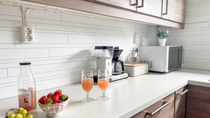 A kitchen with white subway tiles, wooden cabinets, a coffee maker, a microwave, and a fruit bowl with grapes and strawberries. - Rødehuset by Interhome (Reksteren)