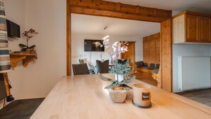 Et moderne køkken med træskabe, et spisebord med stole og et fjernsyn ophængt på væggen.