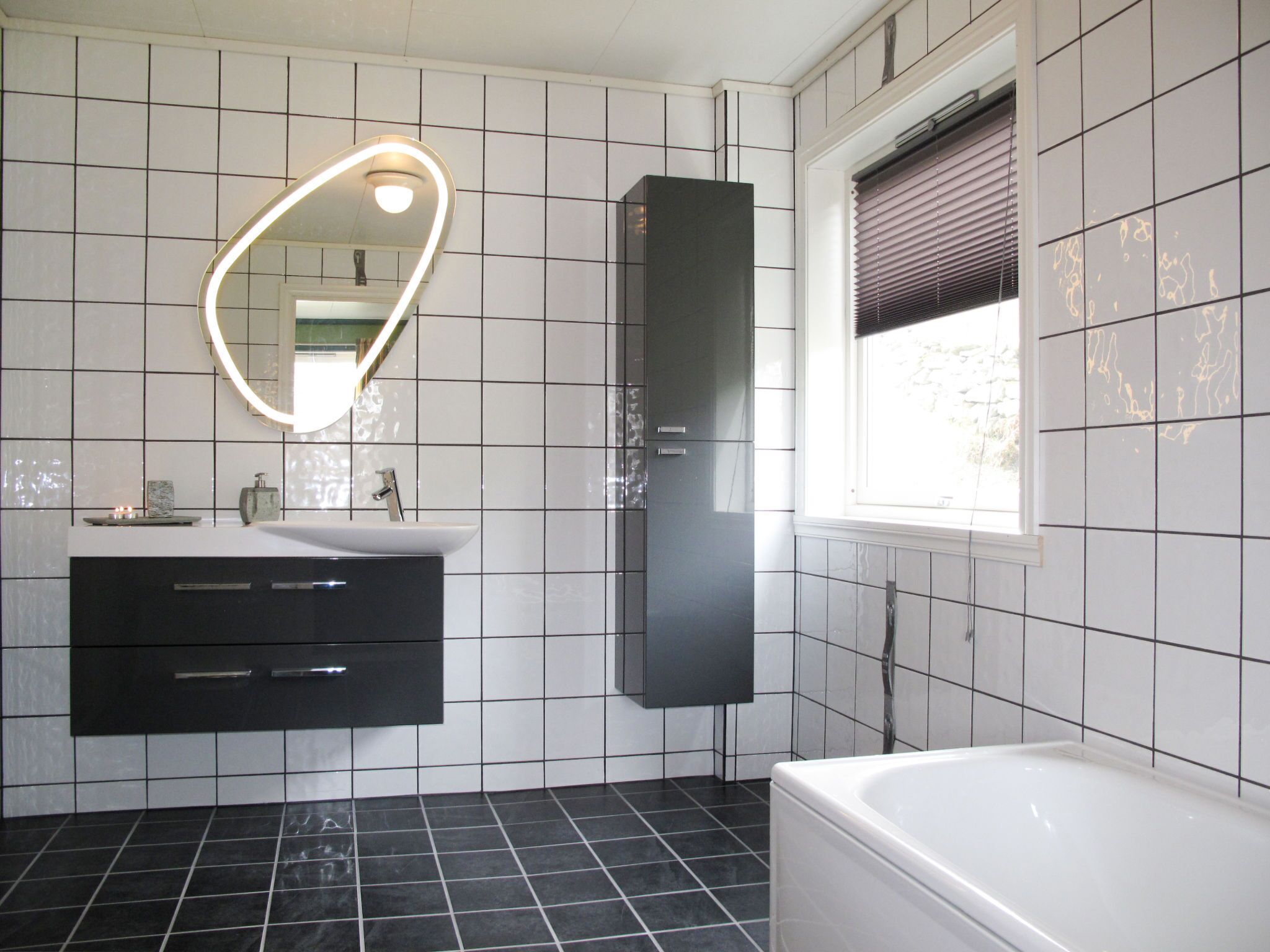 Une salle de bain avec un lavabo blanc, un meuble noir et une baignoire.