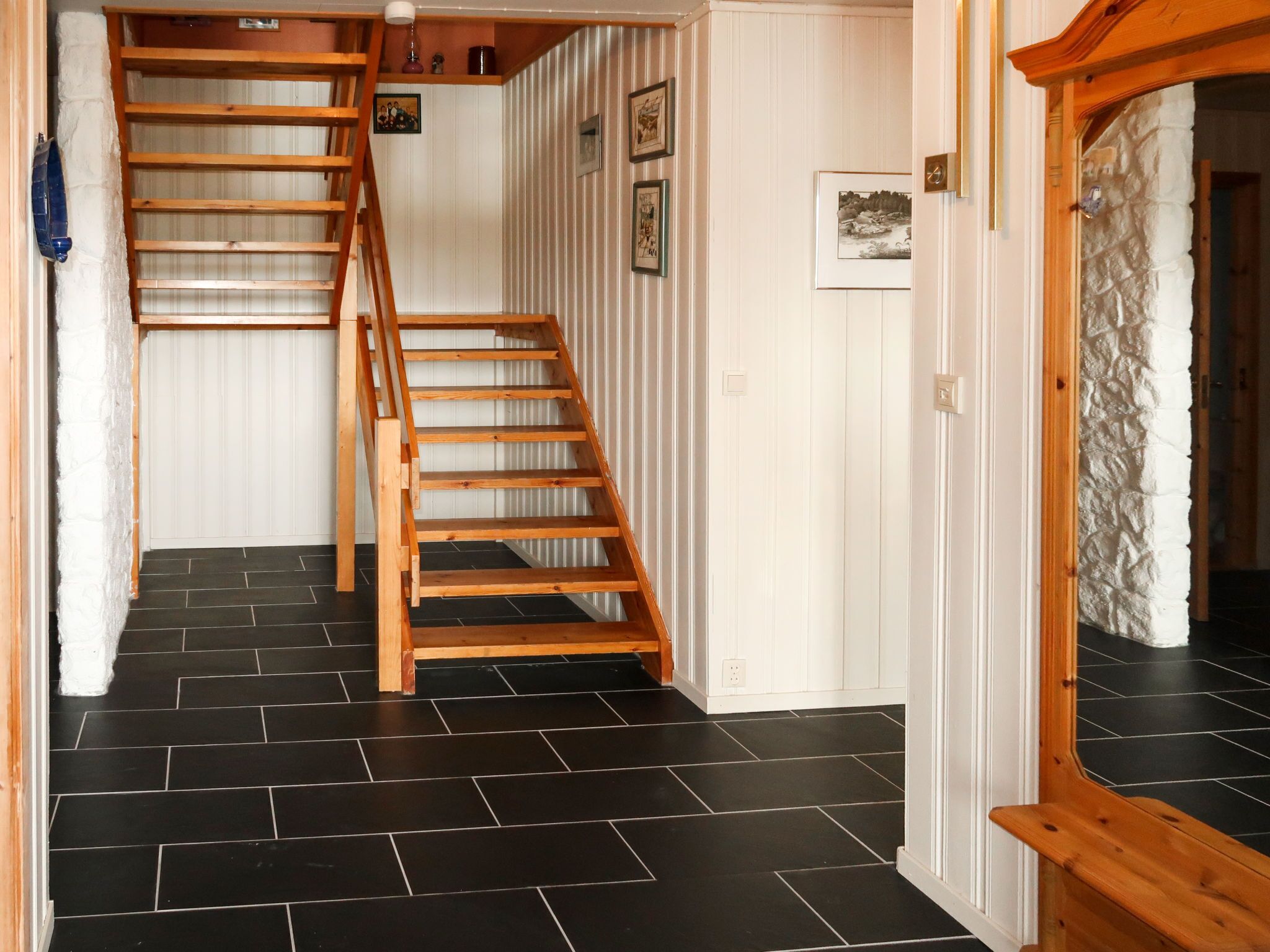 Eine Holztreppe führt zu einem Raum mit weiß gepaneltem Mauerwerk und schwarzem Fliesenboden.