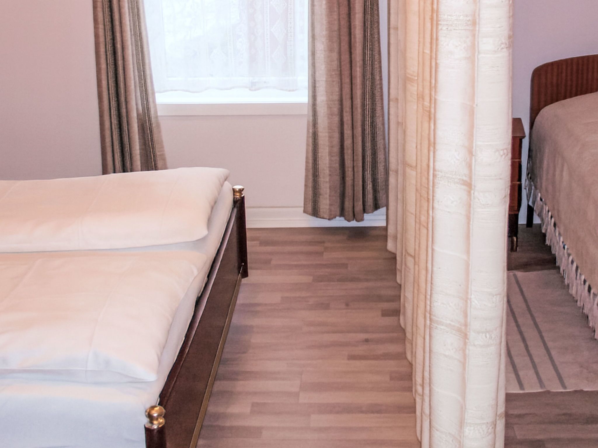 A bedroom with a wooden bed, a window with curtains, and a carpeted floor.