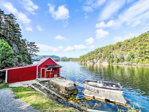 Eine rote Holzhütte am Ufer eines stillen Sees, mit einem Steg, der sich ins Wasser erstreckt.