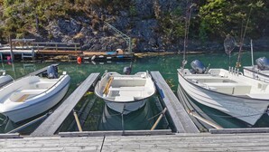 Une jetée en bois où sont amarrées trois embarcations, située dans une marina et entourée de falaises rocheuses et de verdure.