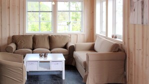 Une pièce chaleureuse avec un canapé beige, une table basse blanche et deux fenêtres donnant sur un paysage verdoyant.