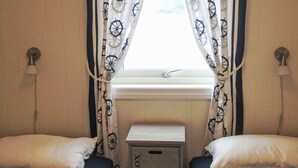 A room with two beds, each with a pillow and a headboard, and a window with curtains. There are two storage boxes labeled 'BOX NO.1' and 'BOX NO.2' against the wall. - Vacation home Tufto by Interhome (Lundegrend)