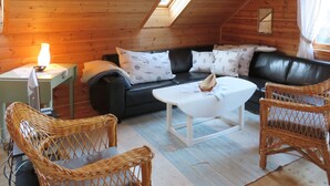 A cozy cabin with a wooden interior, a black leather sofa, wicker chairs, and a small table with a lamp. - Vacation home Tufto by Interhome (Lundegrend)