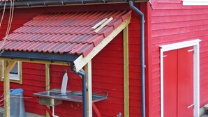 A red building with a metal roof and a small attached structure with a metal table and sink. - Vacation home Tufto by Interhome (Lundegrend)