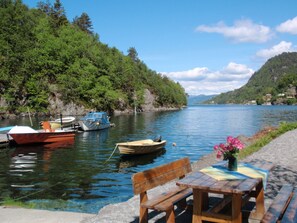 Un lac paisible où sont amarrés des bateaux le long de la rive, entouré d’une végétation luxuriante et de collines.