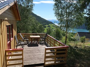 A wooden deck with a table and chairs, overlooking a mountainous landscape and a lake.