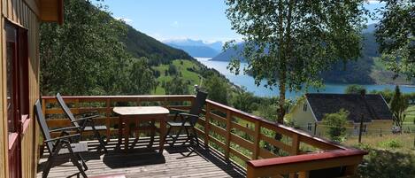 Une terrasse en bois avec une table et des chaises, offrant une vue sur un lac et des montagnes.