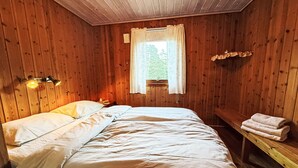 Habitació de fusta amb un llit, una finestra amb cortines, una panxa i una tovallola sobre la panxa.