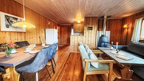 Interior acollidor d'una cabana amb parets i terres de fusta, zona de dinar amb taula i cadires, un sofà i una petita cuina.