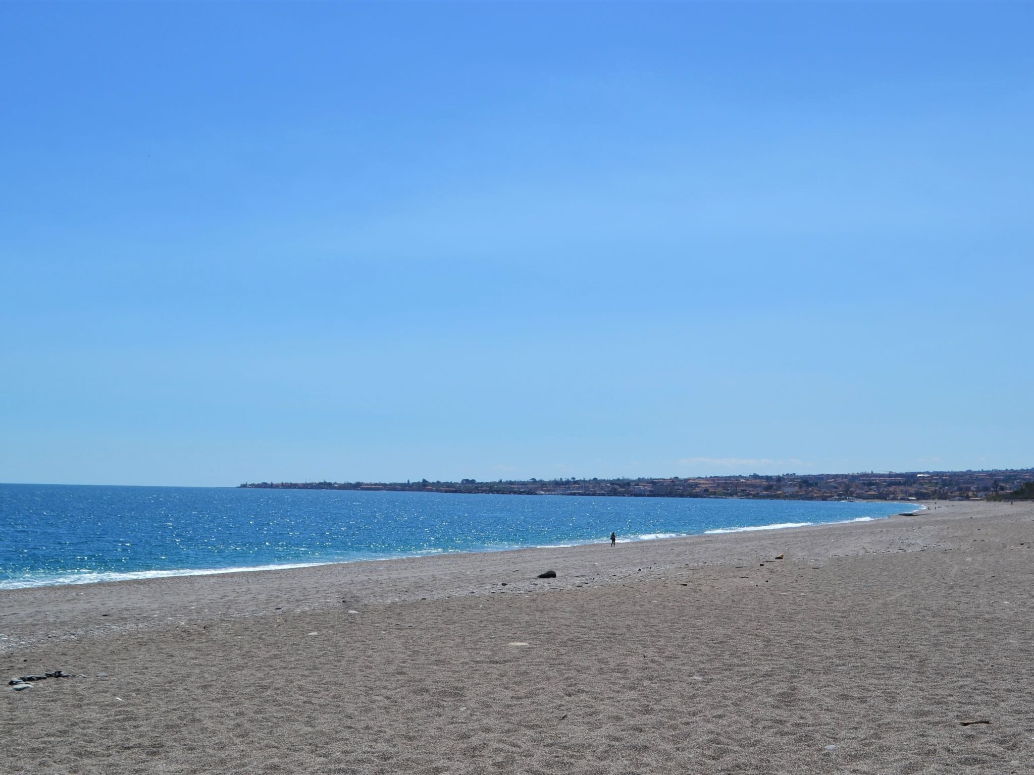 Una playa con cielo despejado, mar tranquilo y edificios al fondo.