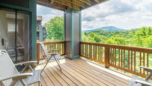 A wooden deck with two chairs and a glass door, overlooking a lush green landscape with mountains in the distance. - Evergreens 1421- Mtn Condo, Gated Resort, Indoor/Outdoor Pools & Hot Tub (Boone)