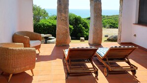 Una terraza con mobiliario de mimbre, un arco de piedra y vista al mar.