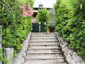 Eine Steintreppe führt zu einem Haus, umgeben von üppigem Grün und einem Metallzaun.