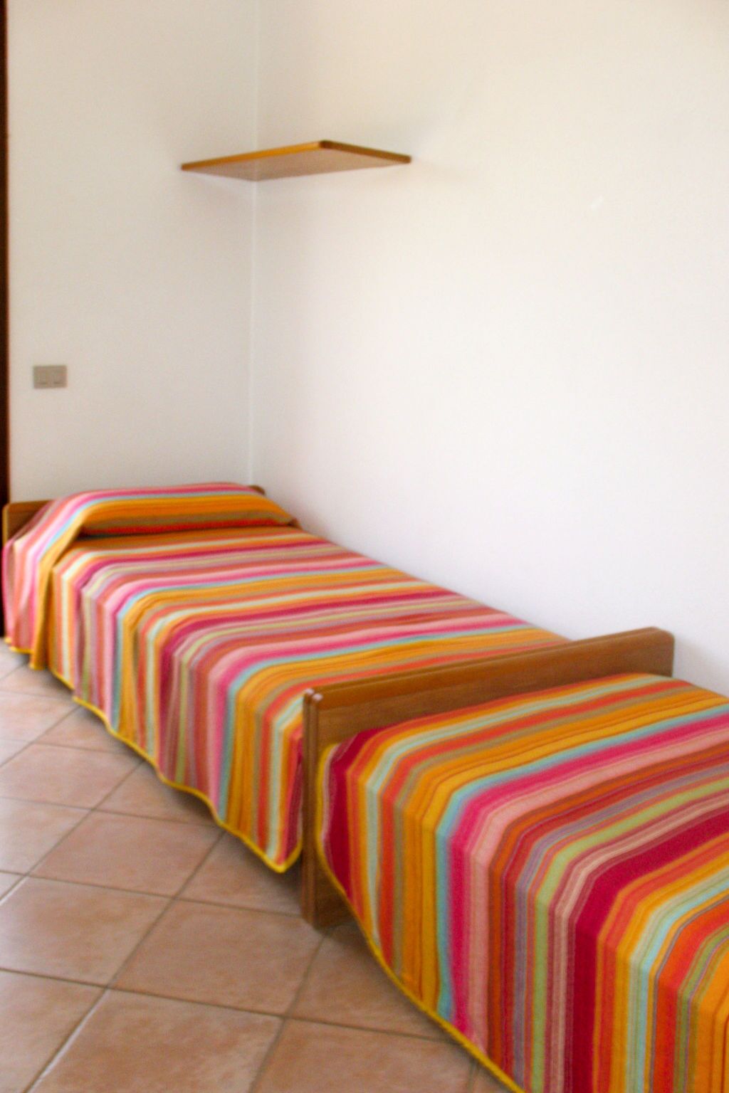 A small, single-bed room with a colorful striped bedspread.