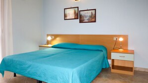 A bedroom with a bed, two bedside tables with lamps, a wooden headboard, and two framed pictures on the wall. - Su Tramatzu (PCR105) by Interhome (Porto Corallo)