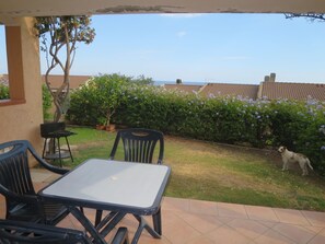 A patio with a table and chairs, a dog, and a view of a garden with a tiled roof in the background. - Su Tramatzu (PCR104) by Interhome (Porto Corallo)