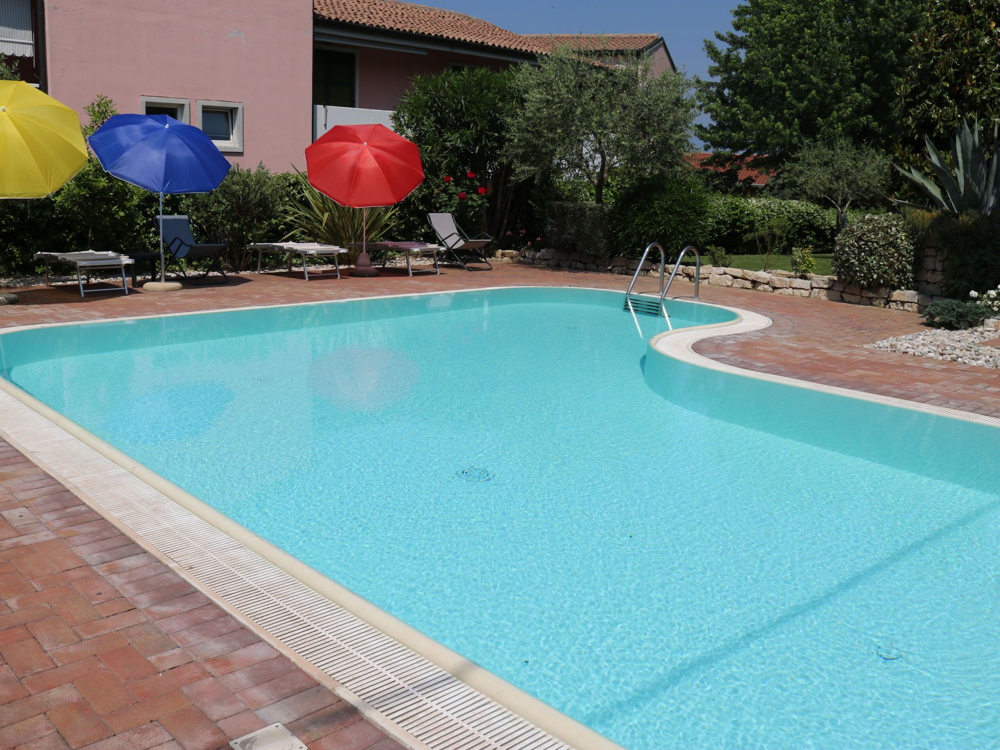 A clear blue swimming pool with a tiled deck, surrounded by lounge chairs and umbrellas.