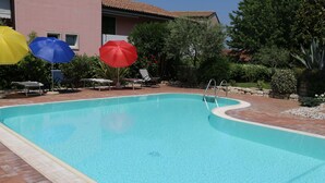 A clear blue swimming pool with a tiled deck, surrounded by lounge chairs and umbrellas.