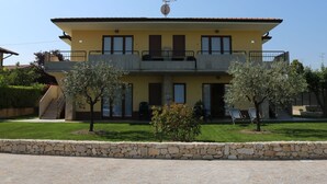 A two-story building with a yellow facade, a balcony on the upper floor, and a stone wall in front.