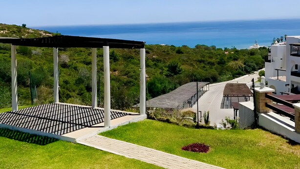 Un espace extérieur moderne agrémenté d’une pergola, d’un chemin pavé et offrant une vue sur la mer.