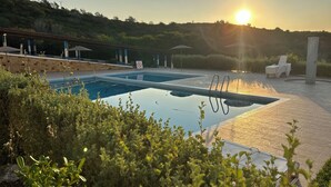Une piscine avec un panneau indiquant qu'il est interdit de se baigner, entourée de verdure et avec un coucher de soleil en arrière-plan.