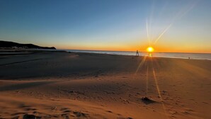 Une plage au coucher du soleil, avec une tour de surveillance et des empreintes de pas dans le sable.