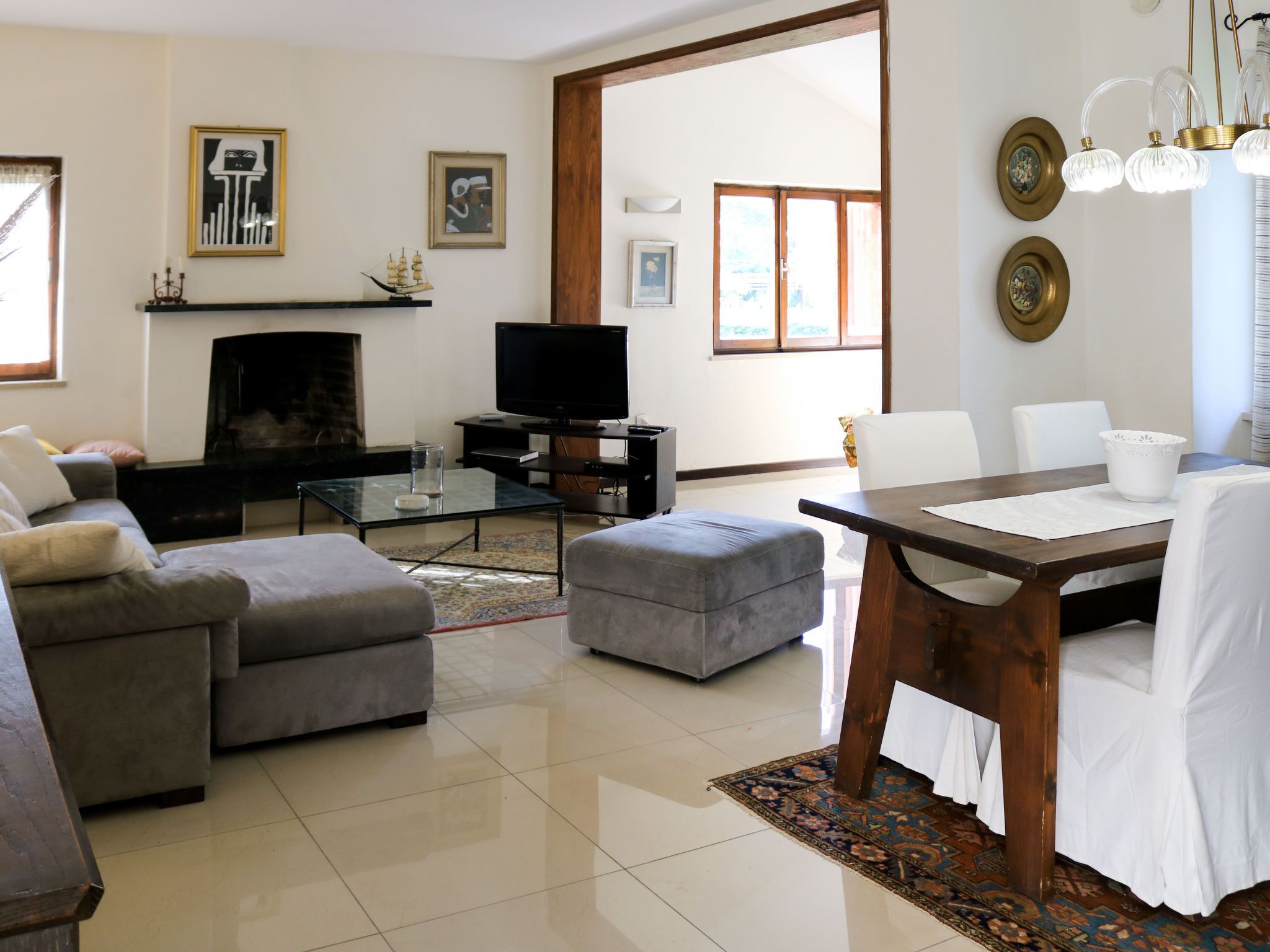 A living room with a fireplace, television, sofa, ottoman, and dining table.
