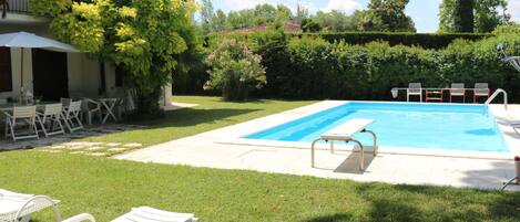 A swimming pool with a sun lounger, a table with chairs, and a building with a balcony.