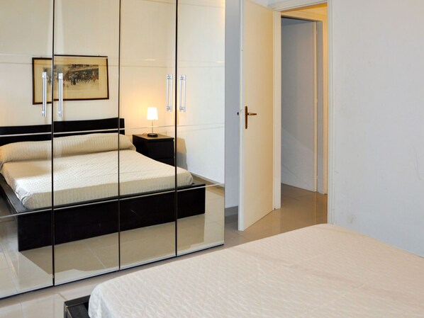 A bedroom with a bed, a nightstand, a lamp, and a door leading to another room.