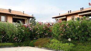 Ein Wohngebiet mit zwei Häusern, jedes mit einem Ziegeldach und einem Schornstein. Vor den Häusern befindet sich ein Garten mit verschiedenen Pflanzen und Blumen.