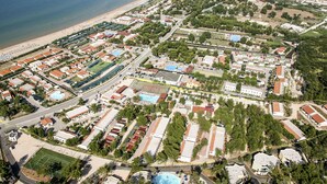 Vista aérea de uma cidade costeira com praia, áreas residenciais e um grande complexo esportivo.