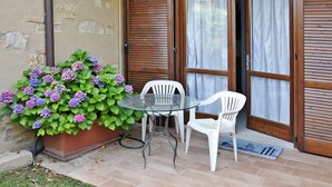 A patio with a glass table and two white chairs, a potted hydrangea plant, and a wooden door with a curtain. - La Casara B by Interhome (Lazise)