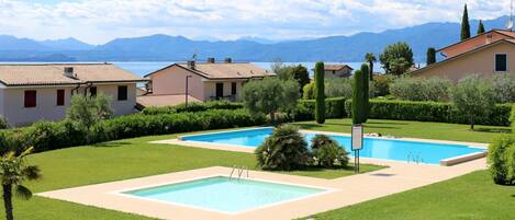 A residential area with two swimming pools, well-maintained lawns, and houses with red-tiled roofs.