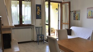 Ein Zimmer mit Holztisch, zwei Stühlen, einer Couch, einem Heizkörper und einem fenster mit Vorhängen.