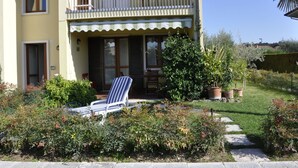 Ein zweistöckiges Gebäude mit Balkon, überdachter Terrasse und Garten mit verschiedenen Pflanzen und einem Stuhl.