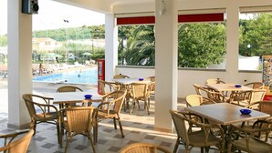 Un restaurant doté d’une terrasse offrant une vue sur une piscine, ainsi que sur des maisons et de la verdure.