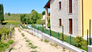 A stone building with a yellow facade, a fenced pool area, and a vineyard path. - I Molini by Interhome (Lazise)