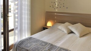Quarto de hotel com uma cama, mesa de cabeceira com abajur, janela com persianas e parede decorada com adesivos de borboletas.