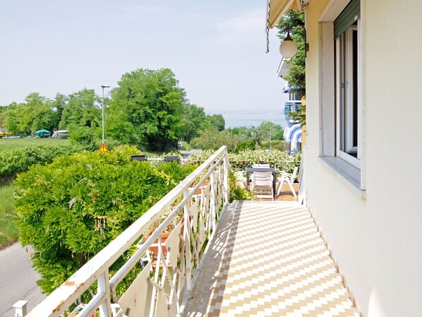 A balcony with a checkered floor, a white railing, and a view of greenery and a building across the street.