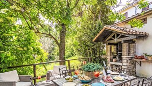 An outdoor dining area with wicker furniture, a stone table, and a view of a building with a tiled roof. - Casa Maja by Interhome (Roccascalegna)