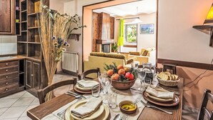 A dining area with a wooden table set for four, a kitchen with dark wood cabinetry, and a living room visible through an open doorway. - Casa Maja by Interhome (Roccascalegna)