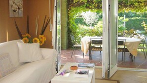 A modern living room with a white sofa, a coffee table with books and a bowl, and a view of an outdoor patio with a table and chairs. - Vacation home Serena by Interhome (Lazise)