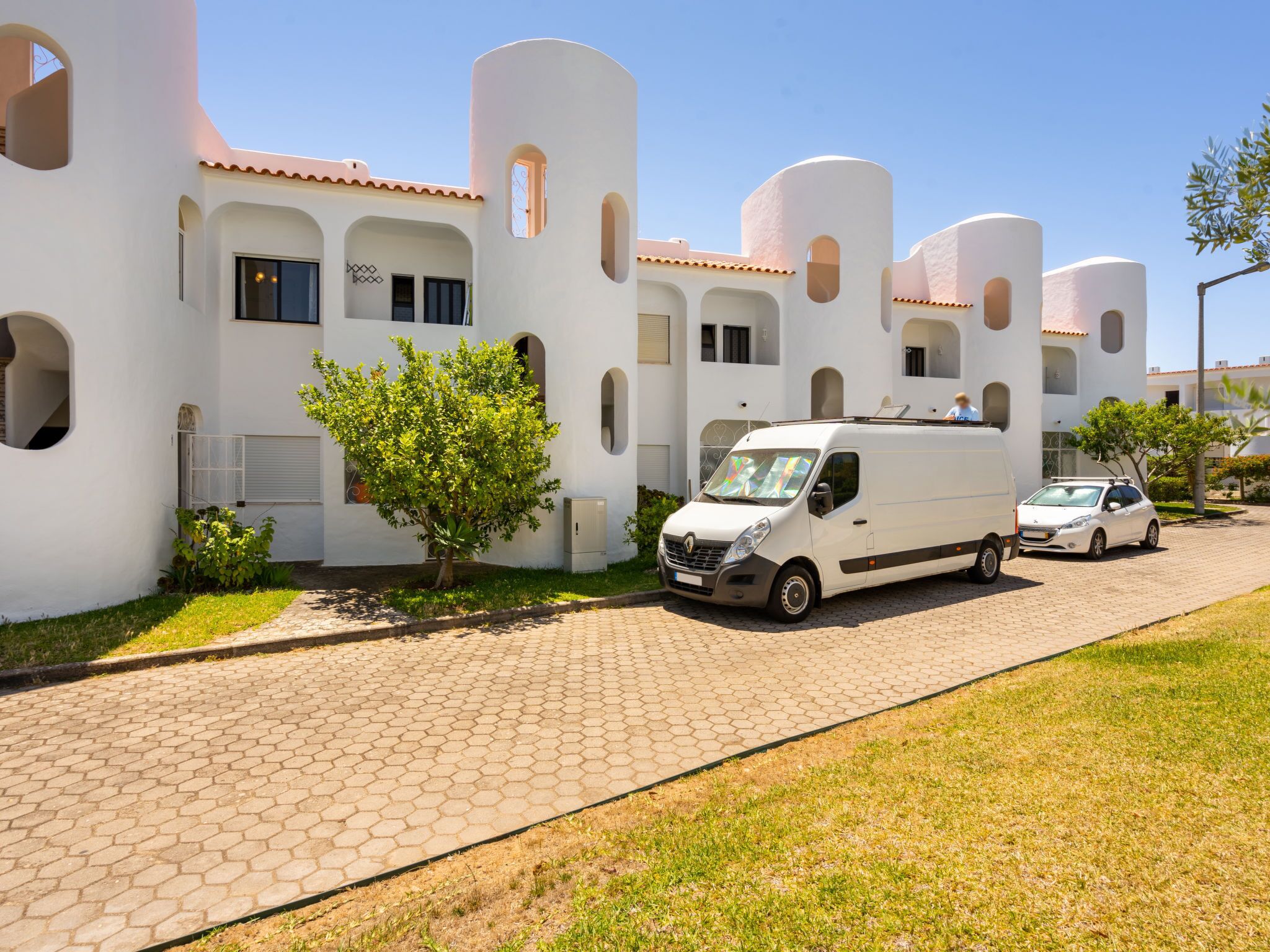 A modern building with white walls and arched windows, a parked van, and a car on a paved driveway.
