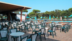 Un espacio al aire libre con mesas, sillas, piscina y sombrillas.