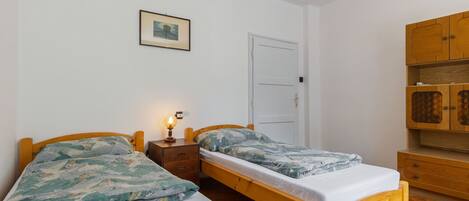 A room with two wooden beds, a small bedside table with a lamp, a white door, and wooden cabinets.