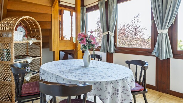 Een eetruimte met een ronde tafel, stoelen, een rieten mand en een vaas met bloemen.